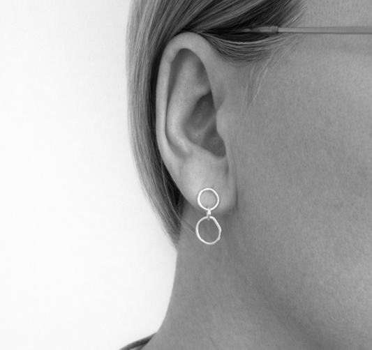 Close-up of an ear wearing a silver hoop earring against a neutral background