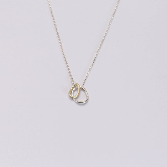 Contour pendant on a delicate sterling silver chain with two interlocking rings — one crafted in 14K gold and the other in sterling silver, inspired by contour lines.”