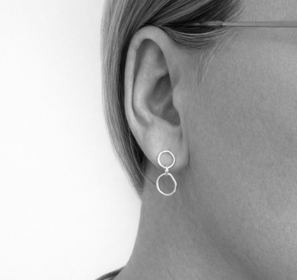 Close-up of an ear wearing a silver hoop earring against a neutral background