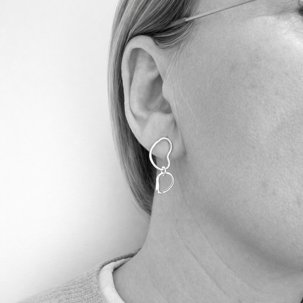 Silver stud earrings worn by a person on a plain background