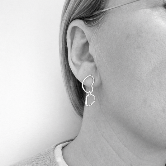 Silver stud earrings worn by a person on a plain background