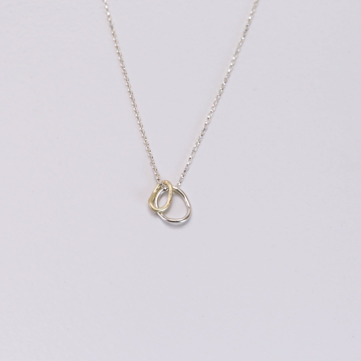 Contour pendant on a delicate sterling silver chain with two interlocking rings — one crafted in 14K gold and the other in sterling silver, inspired by contour lines.”