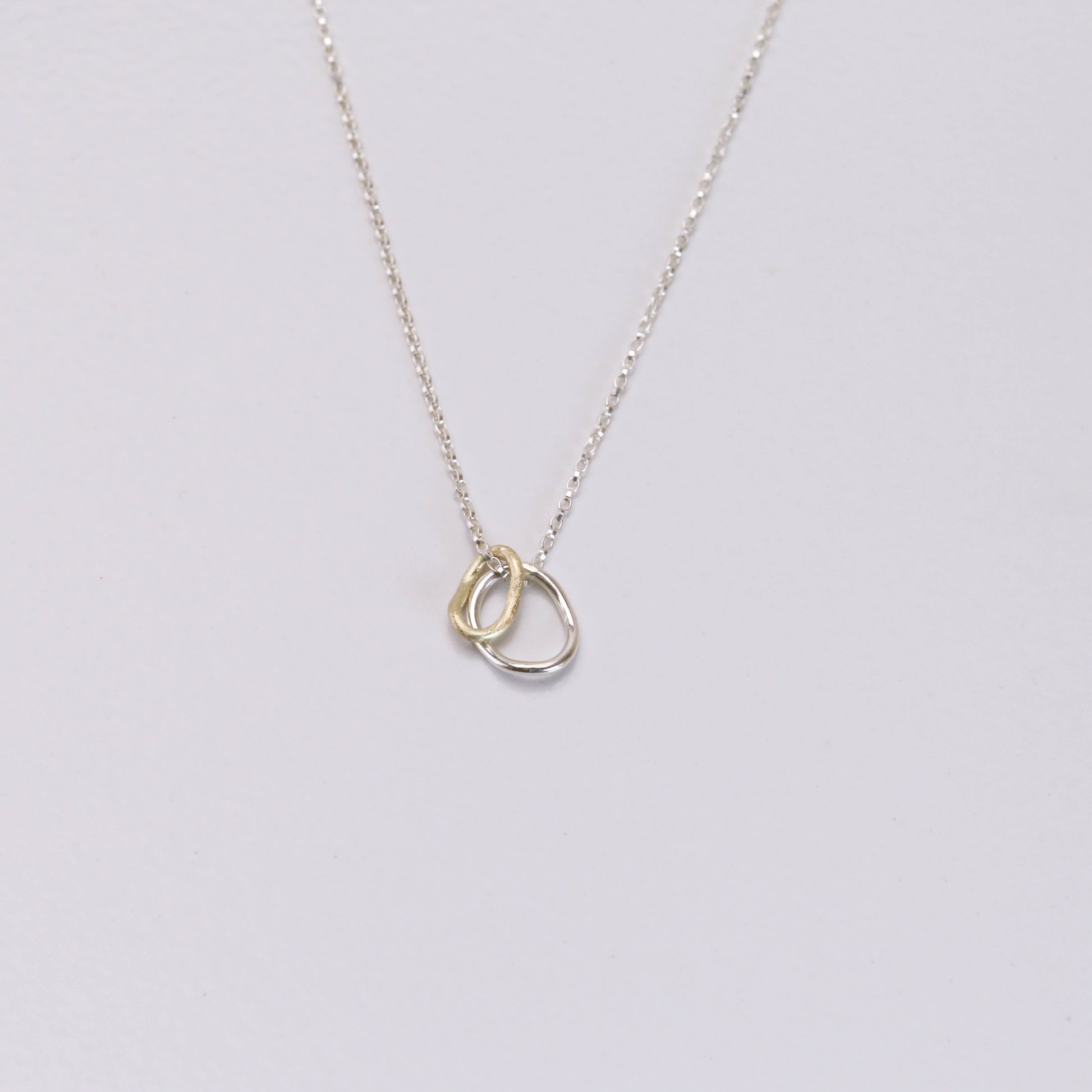 Contour pendant on a delicate sterling silver chain with two interlocking rings — one crafted in 14K gold and the other in sterling silver, inspired by contour lines.”