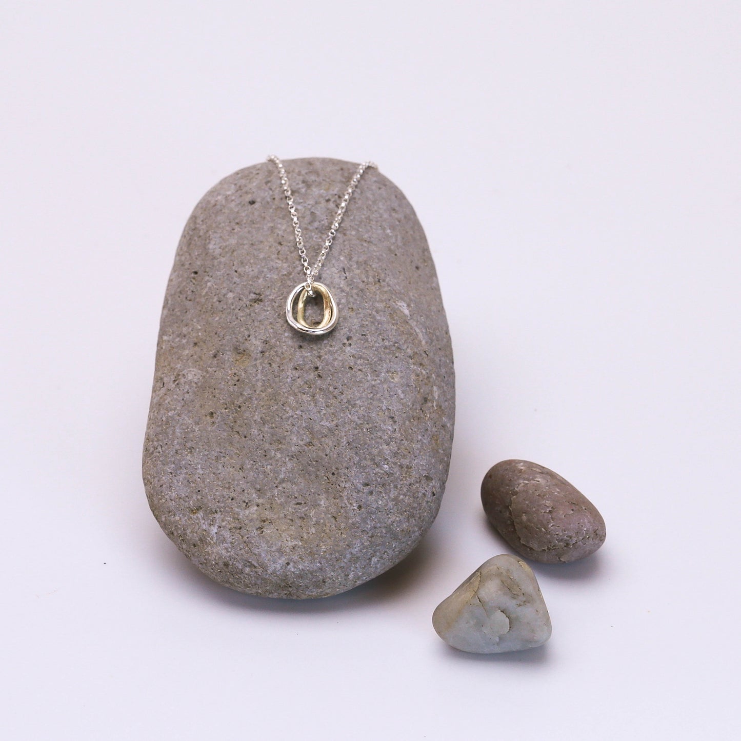 Contour pendant on a delicate sterling silver chain with two interlocking rings — one crafted in 14K gold and the other in sterling silver, inspired by contour lines.”