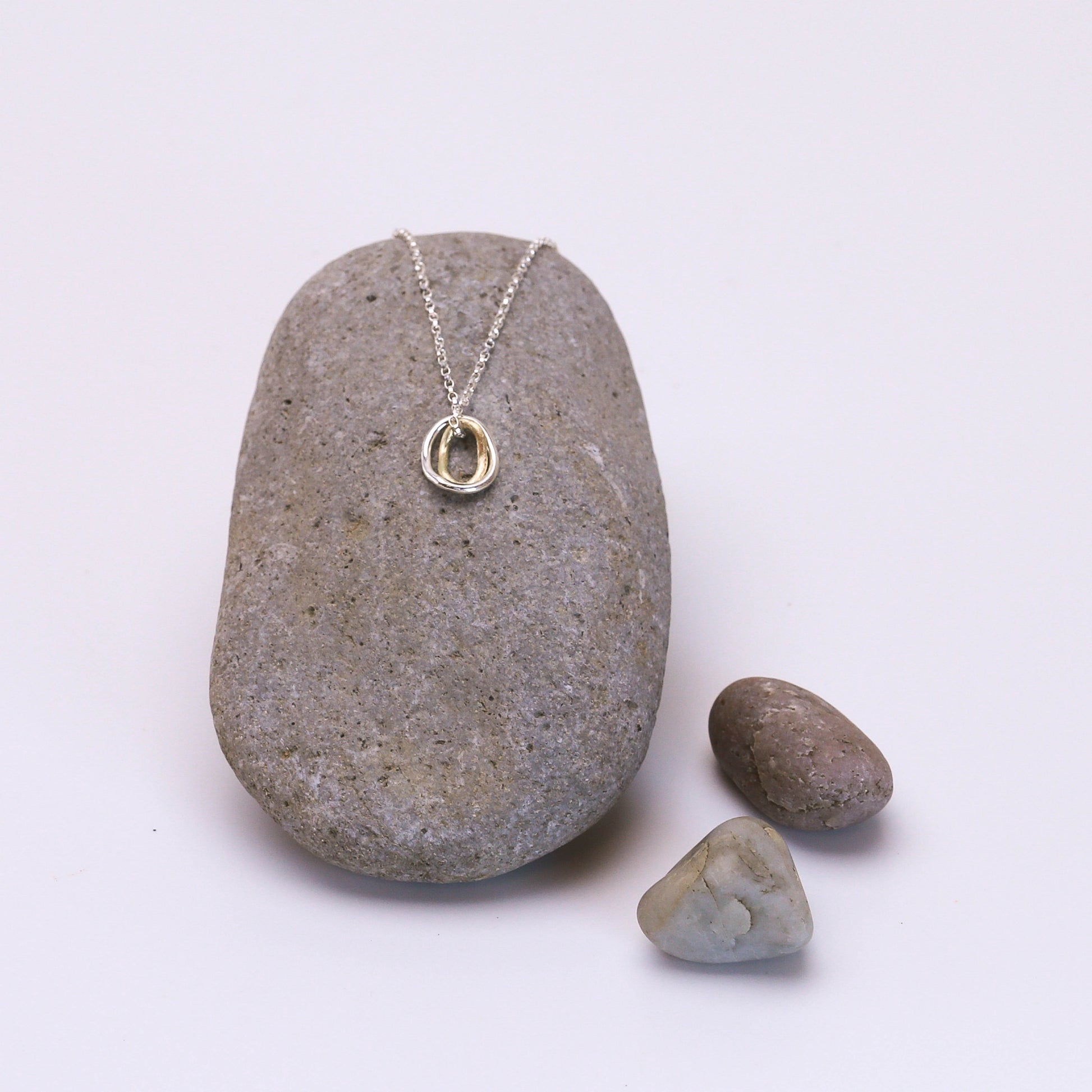 Contour pendant on a delicate sterling silver chain with two interlocking rings — one crafted in 14K gold and the other in sterling silver, inspired by contour lines.”