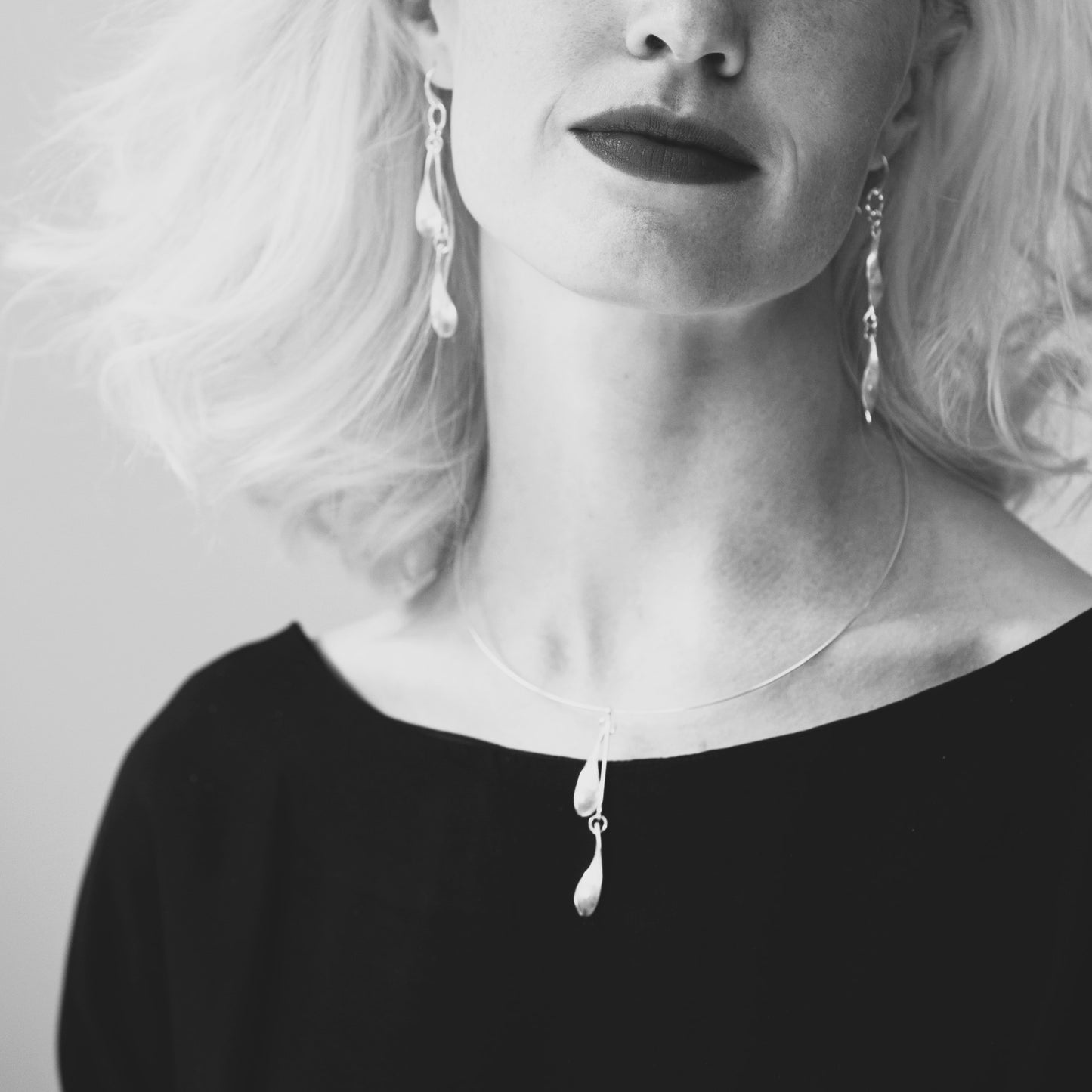 Black and white close-up of a person wearing earrings and a necklace.