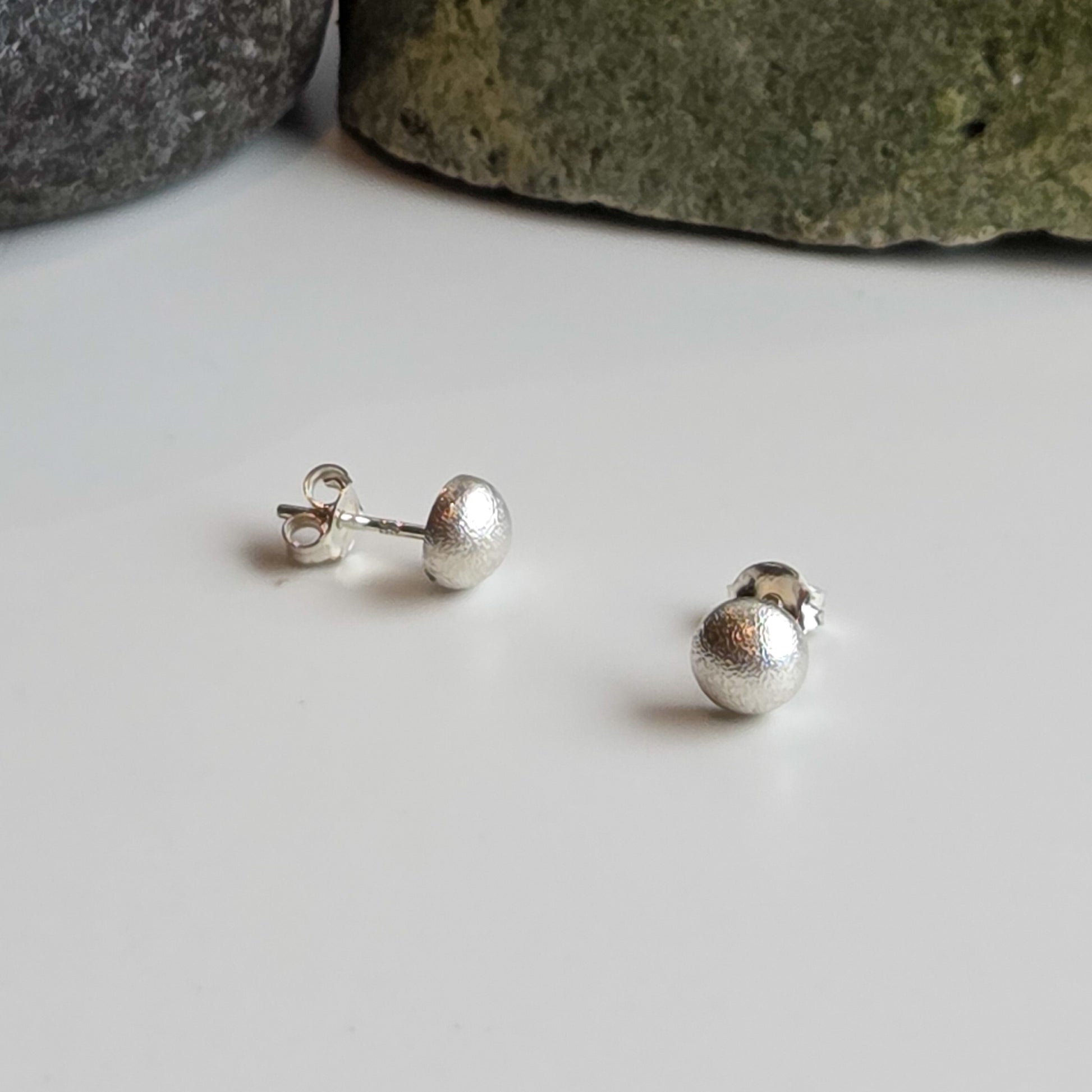 Silver stud earrings on a white surface with stones in the background