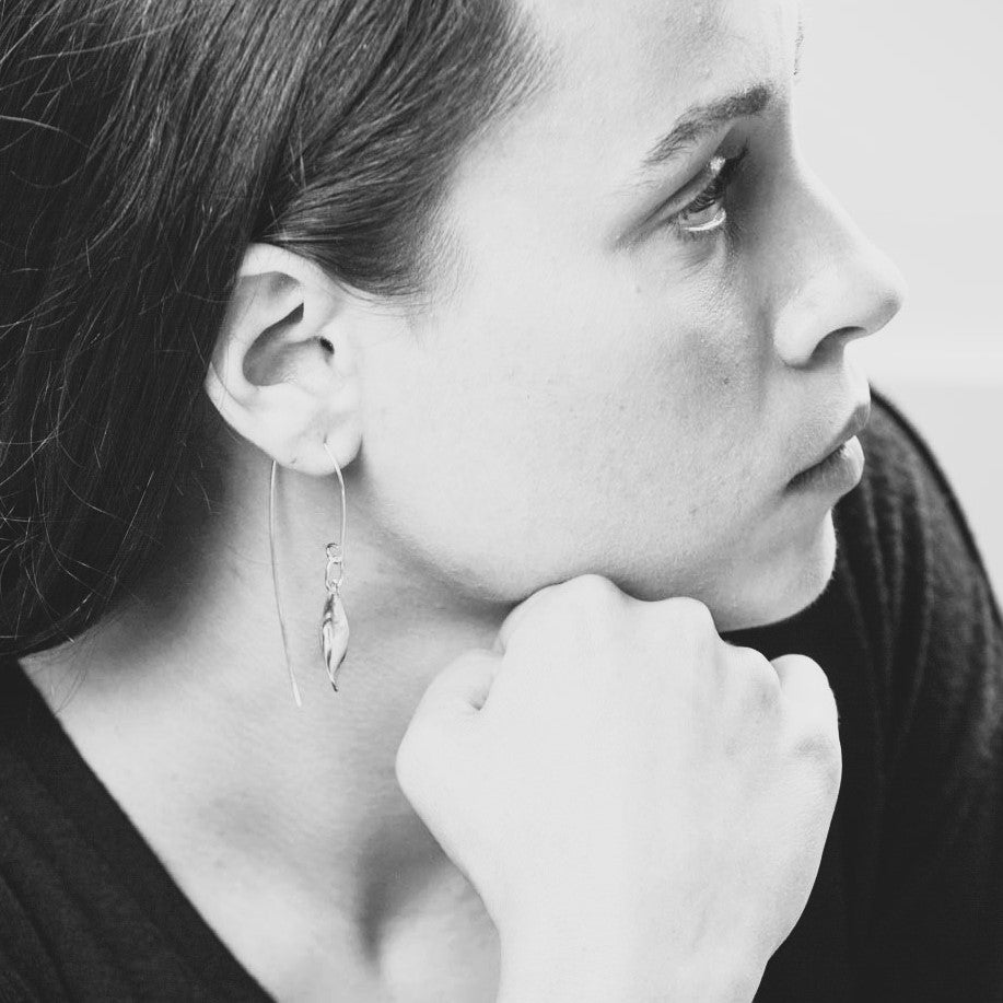 Black and white close-up of a person wearing earrings with a hand on their chin.