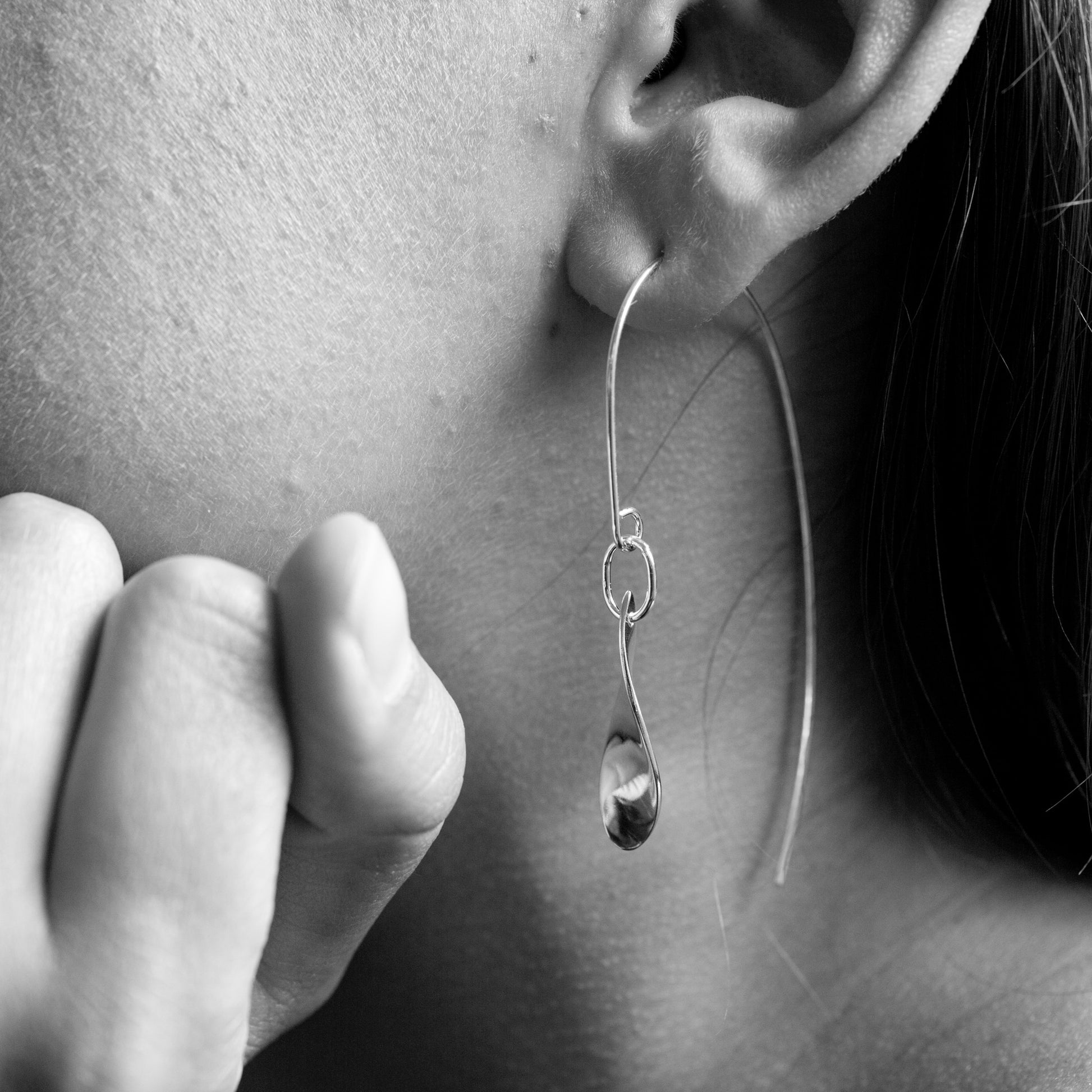 Close-up of a person wearing a silver earring with a teardrop-shaped pendant.