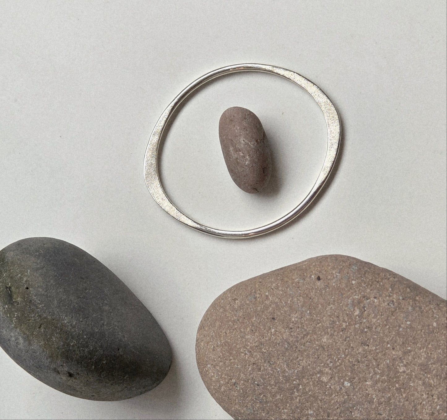 Silver hoop with a stone inside, surrounded by three stones on a light gray background