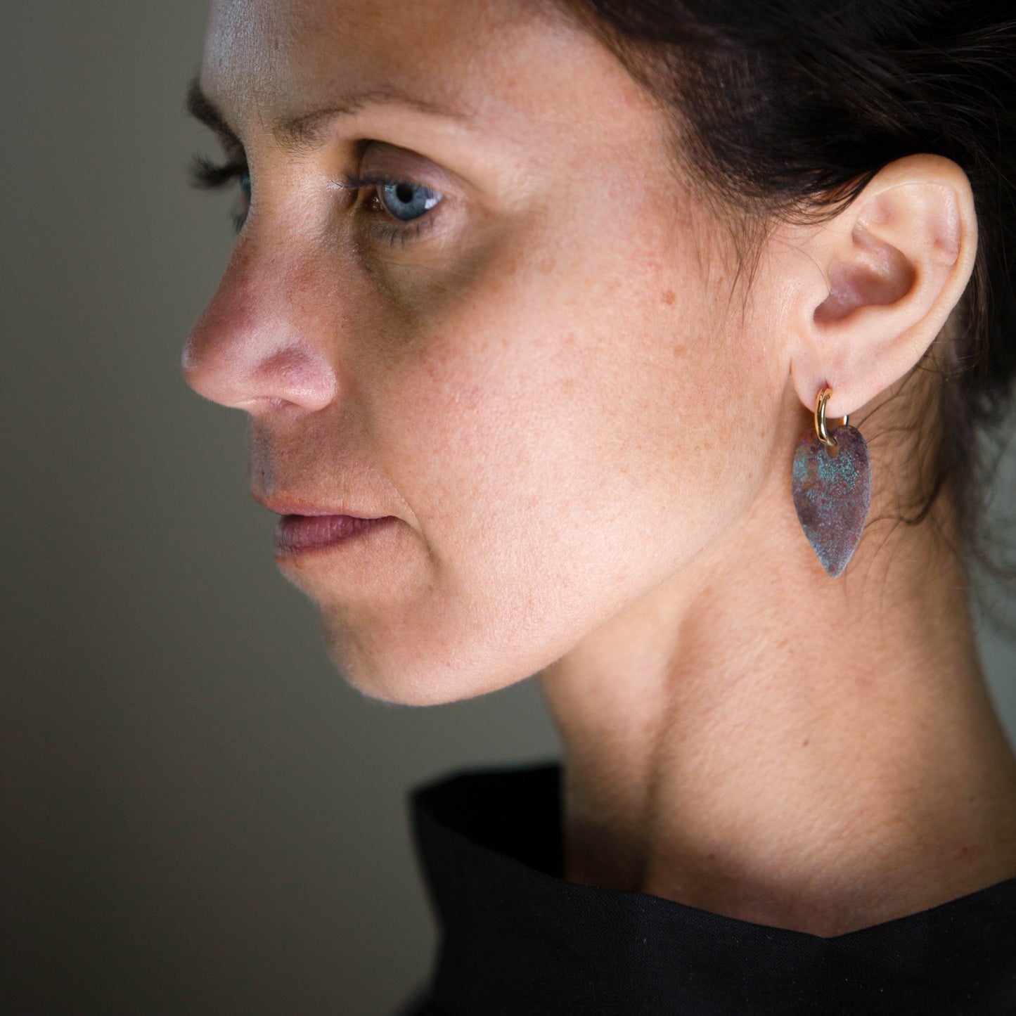 Close-up of a woman wearing a 14K gold fill hoop earring with a patinated copper pendant.