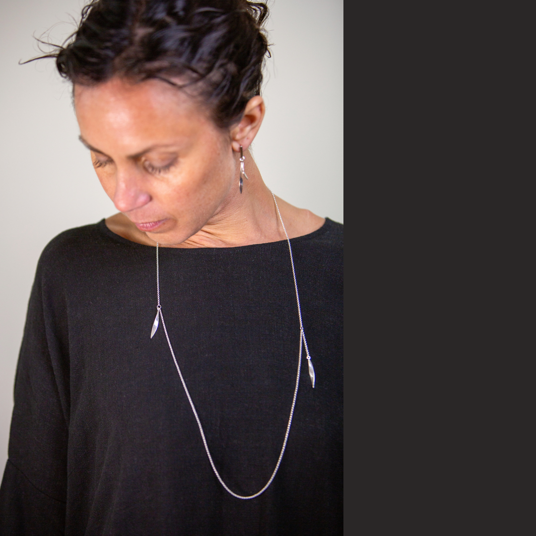 Person wearing a long necklace with feather pendants against a plain background