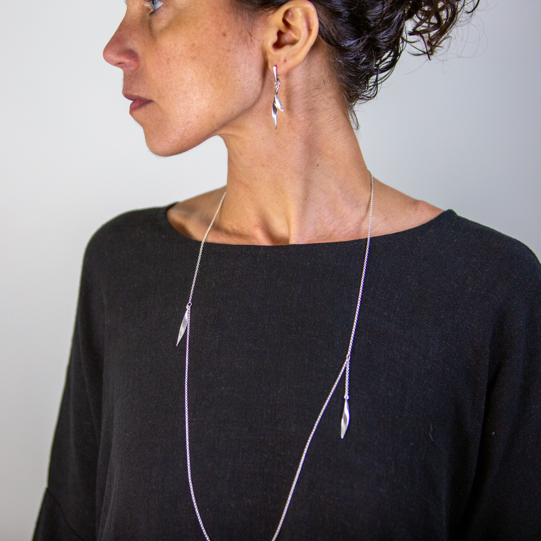 Woman wearing a long necklace and earrings against a plain background