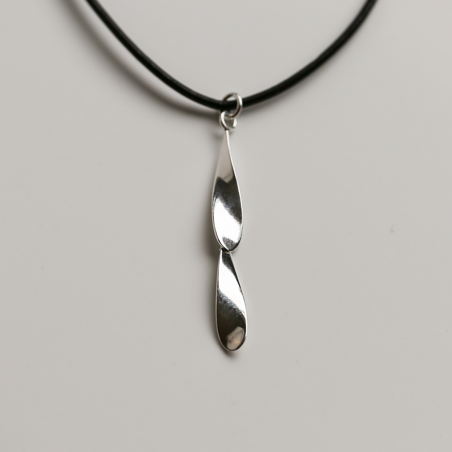 Silver pendant on a black cord against a gray background