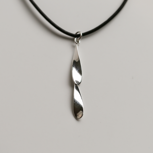 Silver pendant on a black cord against a gray background