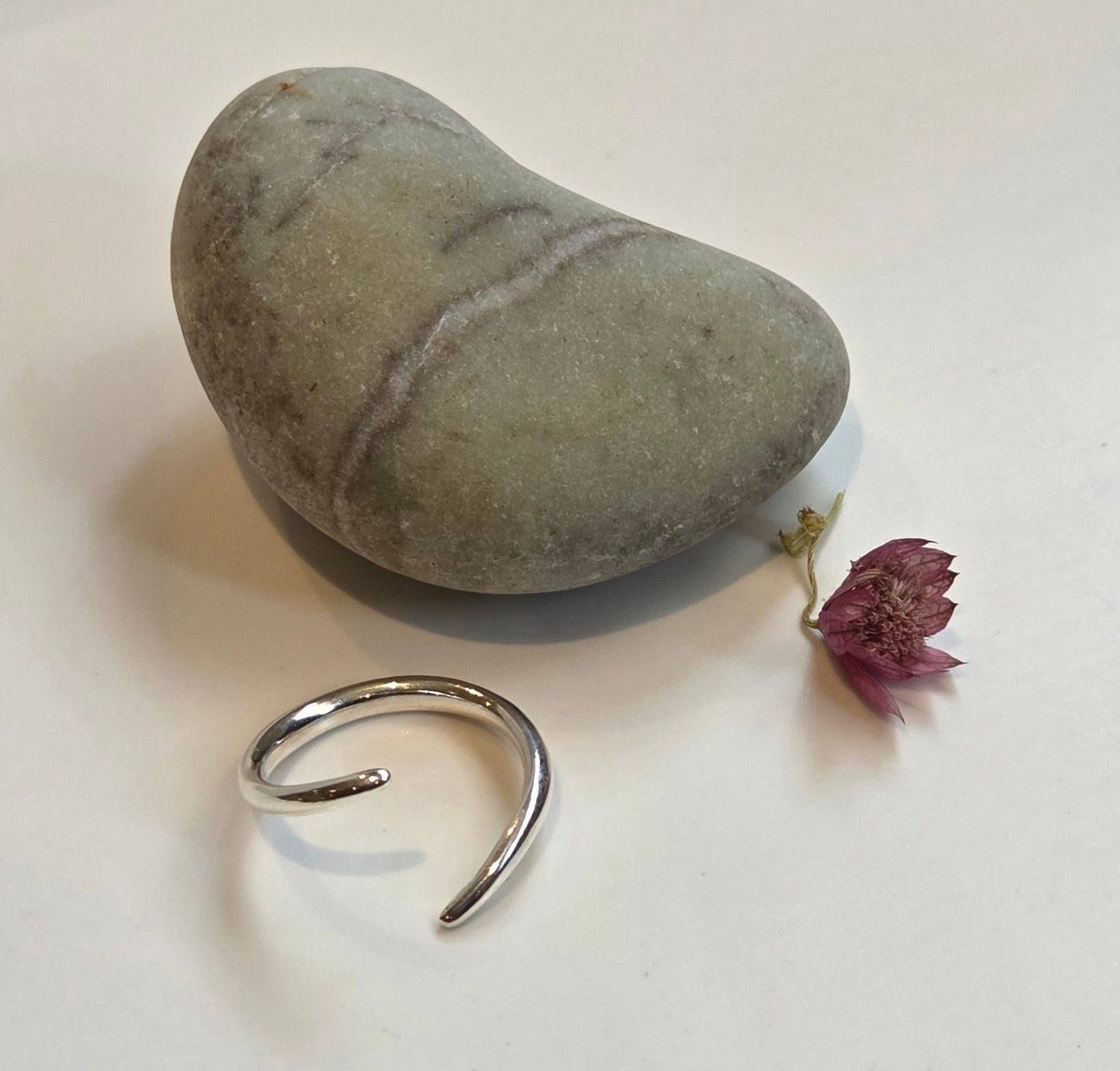 Silver ring on a white surface with a heart-shaped stone and a small purple flower.