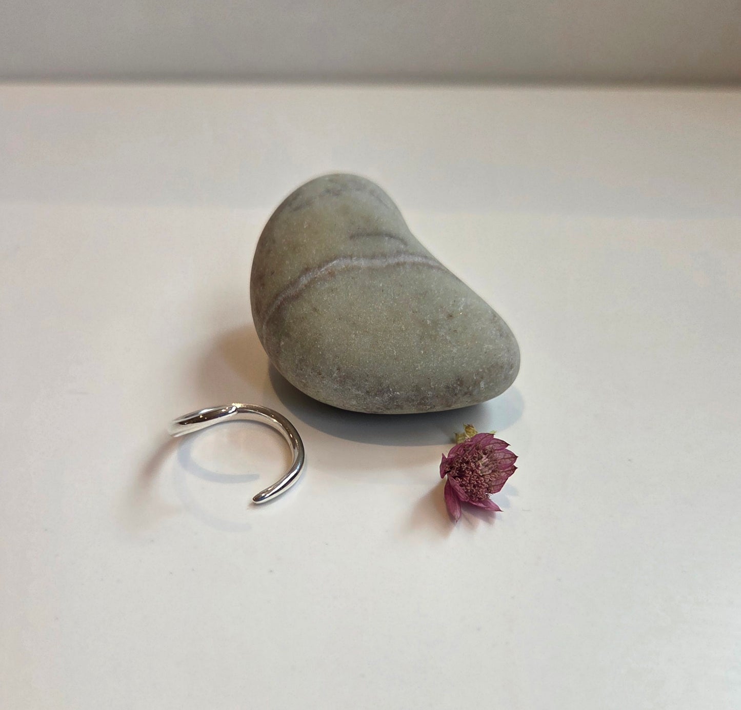 Silver ring, stone, and small purple flower on a white surface